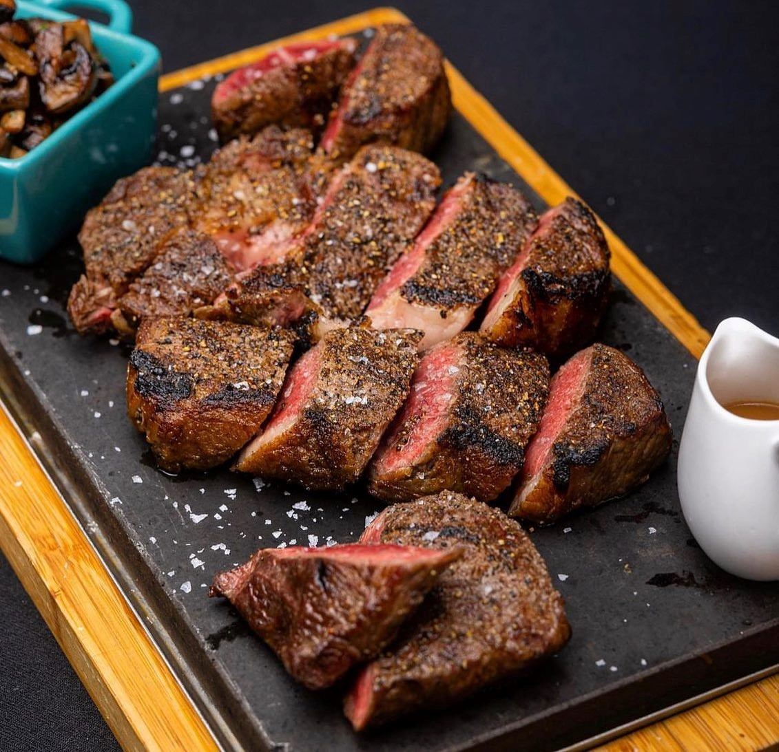 Close-up of a plated steak with garnish and sauce on a dark plate.