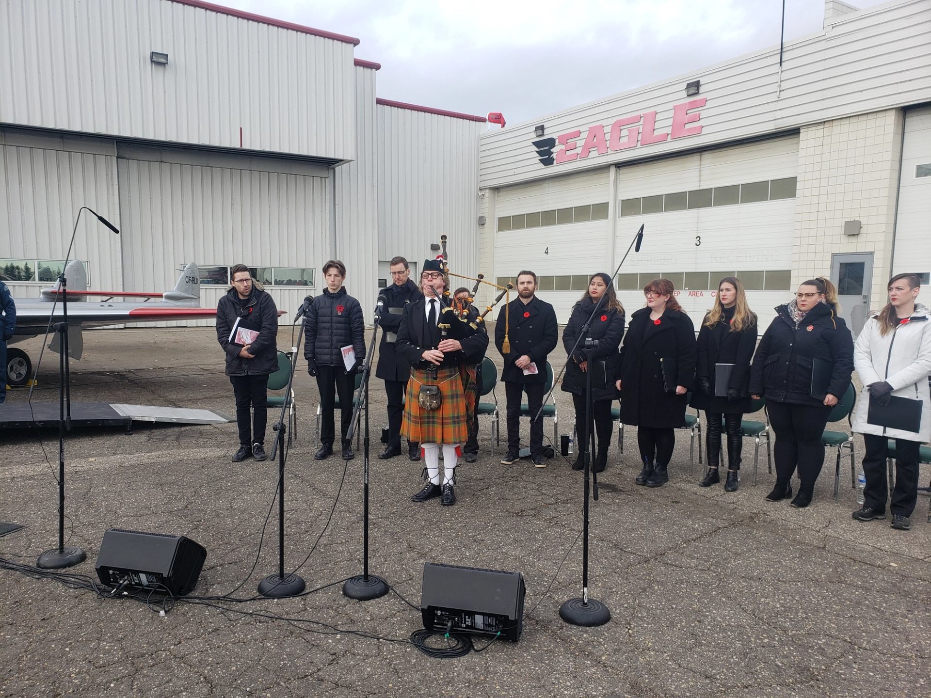 Group standing in formation outdoors near aircraft hangar for Remembrance Day ceremony.