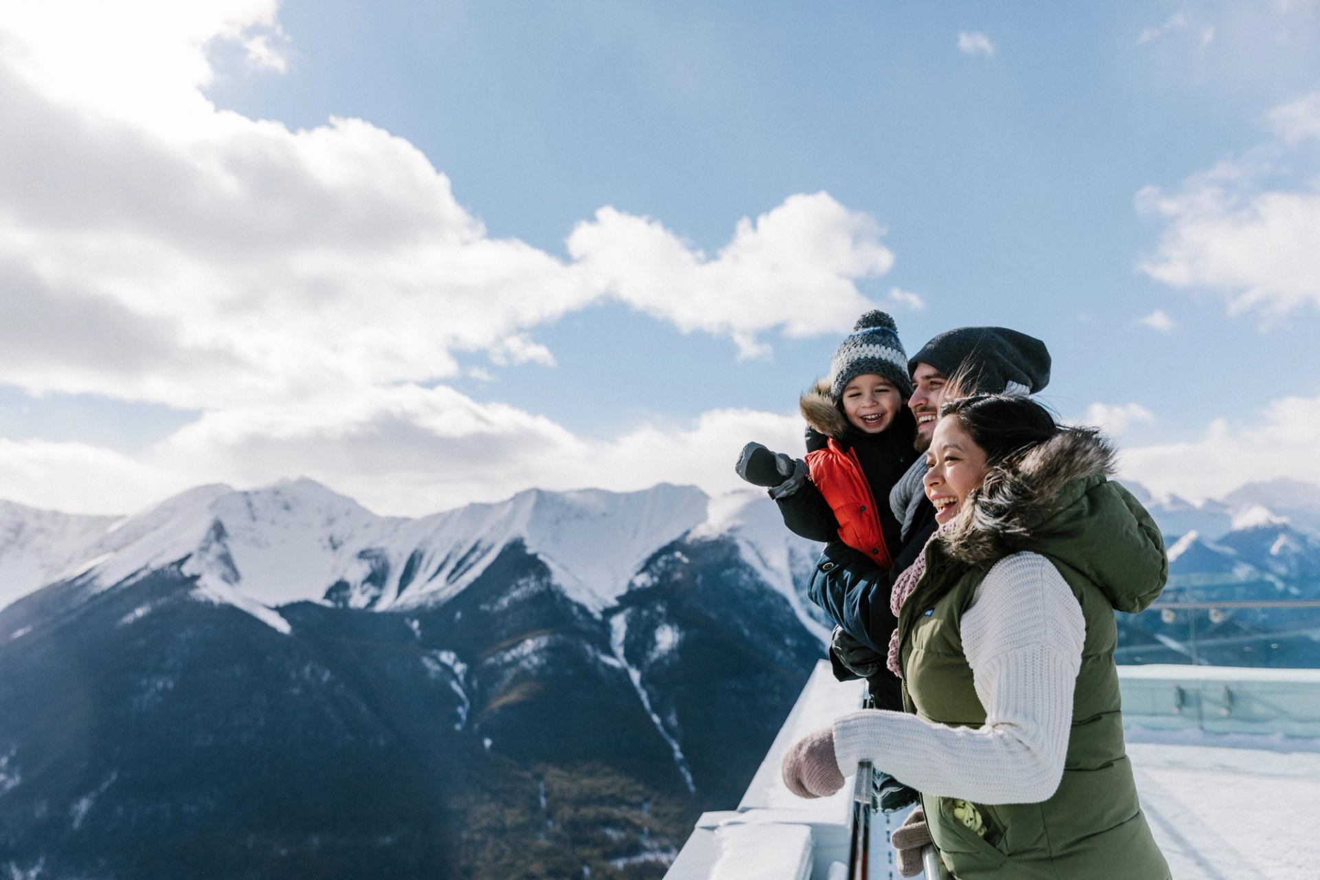 Three people on mountain viewing platform with snowy peaks in the background.