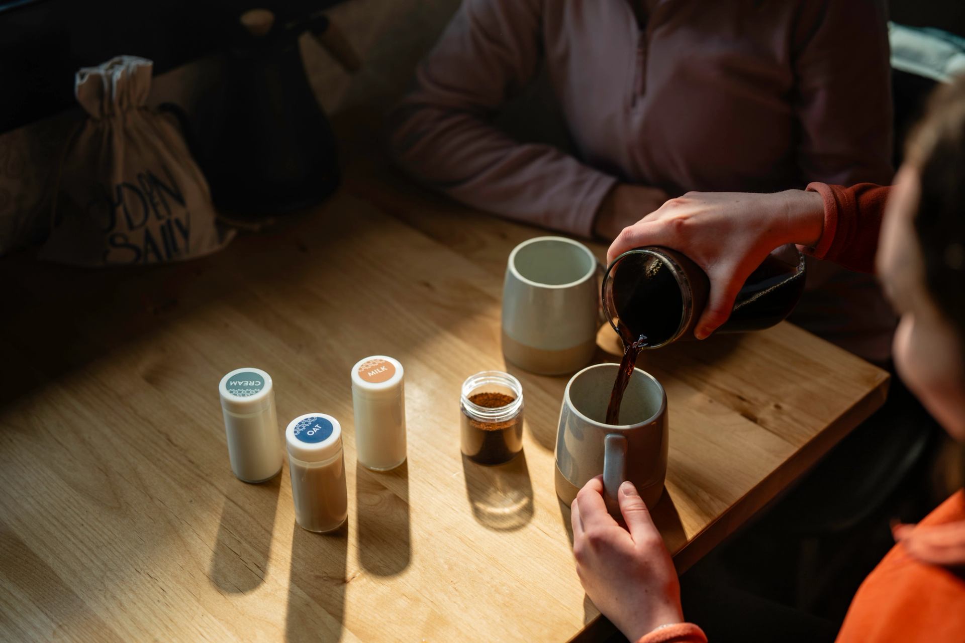 Hand pouring coffee into mug with three milk options in little jars next to it.