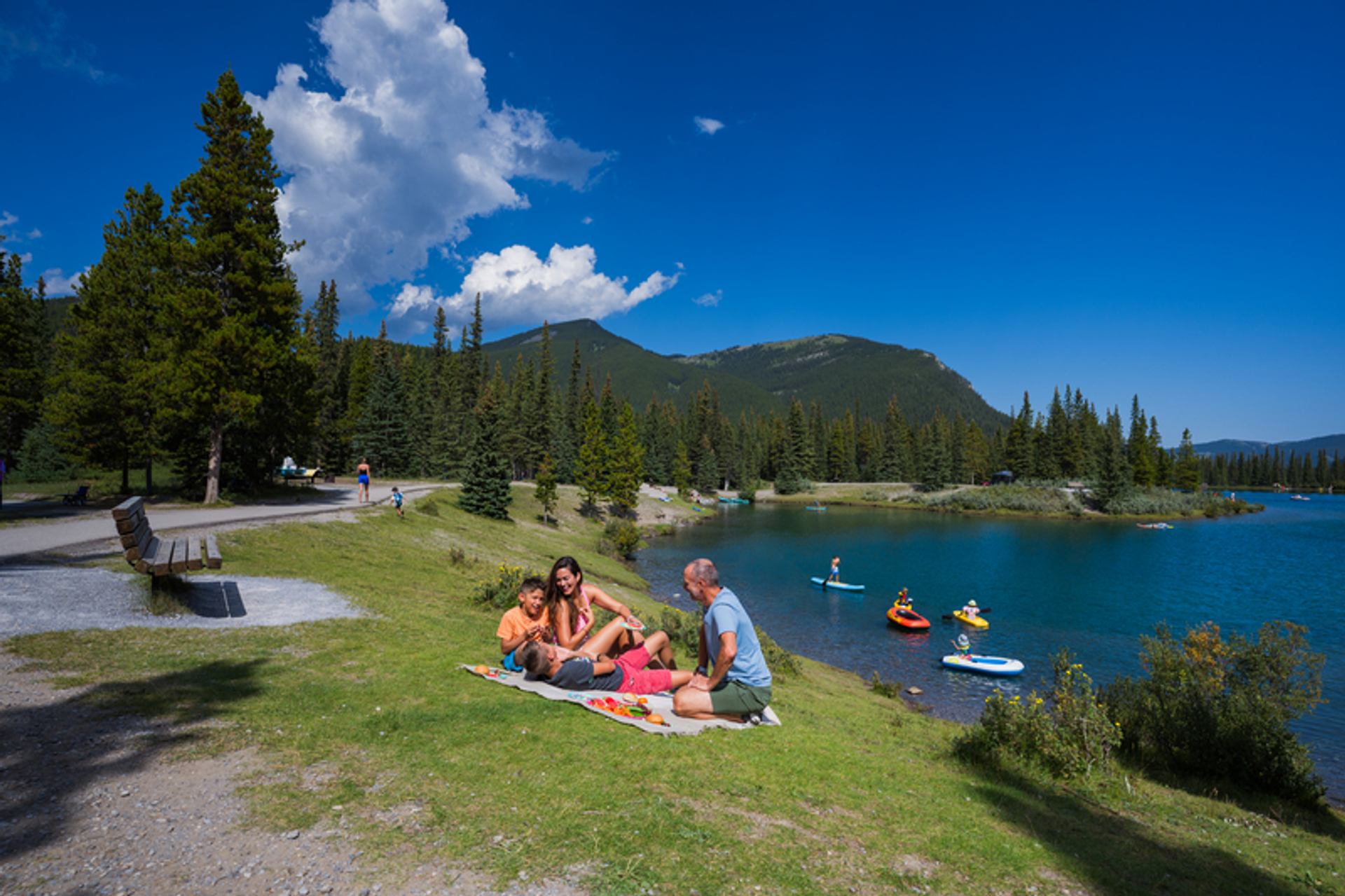 Visitors overlook Forgetmenot Pond where paddlers enjoy calm water beneath forested mountains.