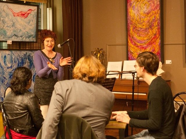 Speaker with mic addresses seated guests in art-filled space at The Carrot.