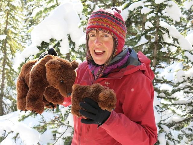 A woman in a red coat holding brown stuffed bear toys.