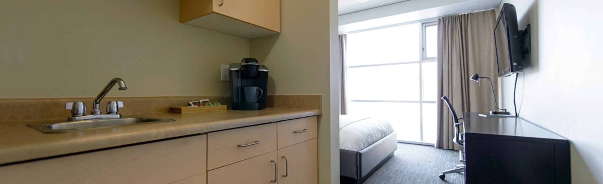 A suite kitchenette includes a sink, coffee maker, workspace, television, and large sunlit window.
