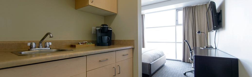 A suite kitchenette includes a sink, coffee maker, workspace, television, and large sunlit window.
