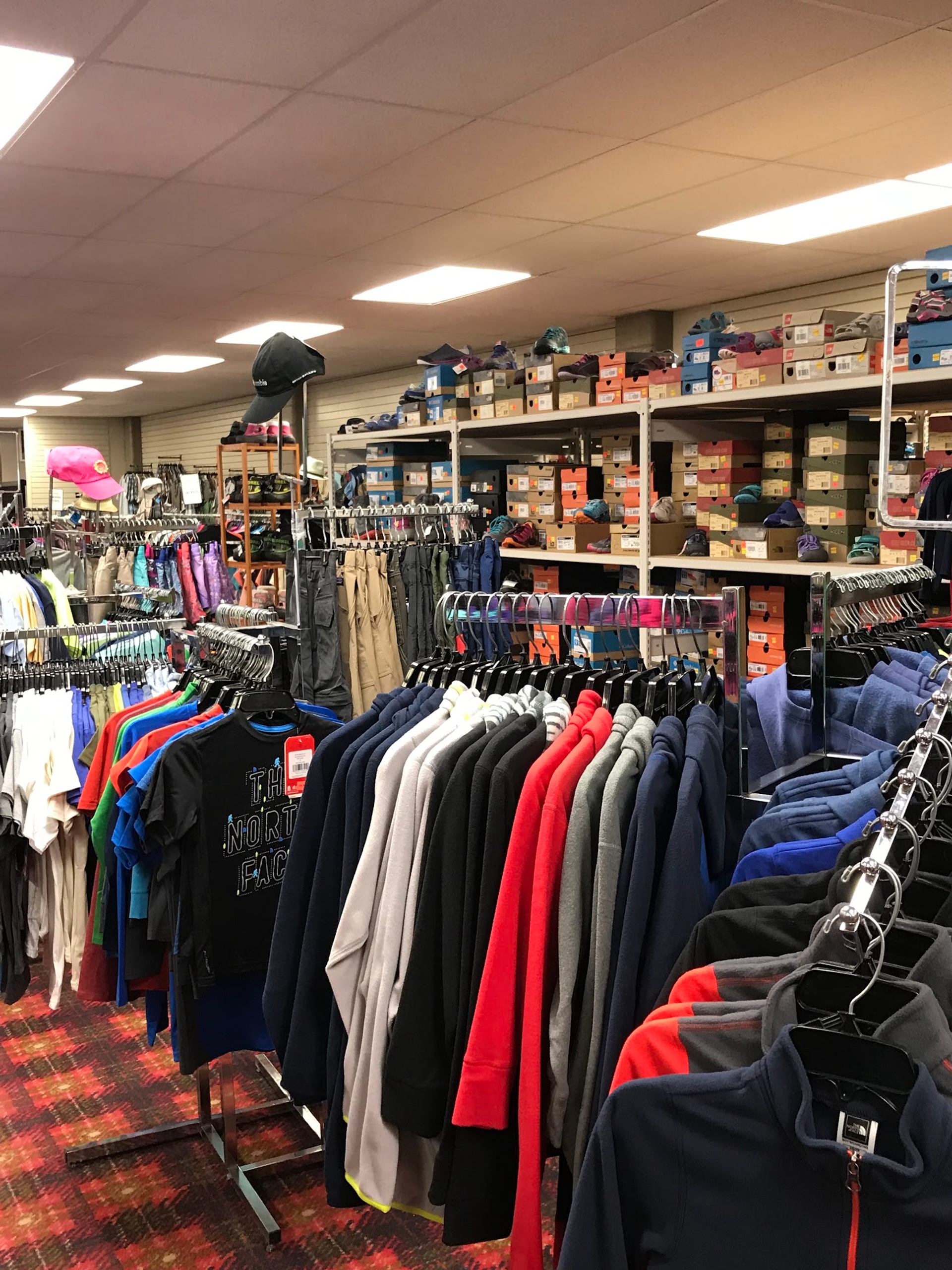 Clothing store interior with racks of jackets and shirts, shelves stacked with shoe boxes.