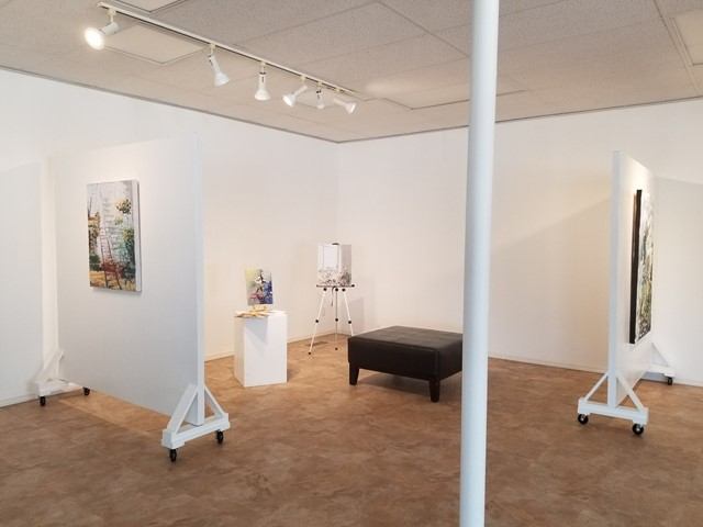 Art gallery room with paintings on display, white partitions, and track lighting on ceilings.