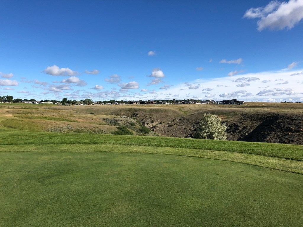 Golf green overlooking a rugged valley under a bright blue sky with scattered clouds.