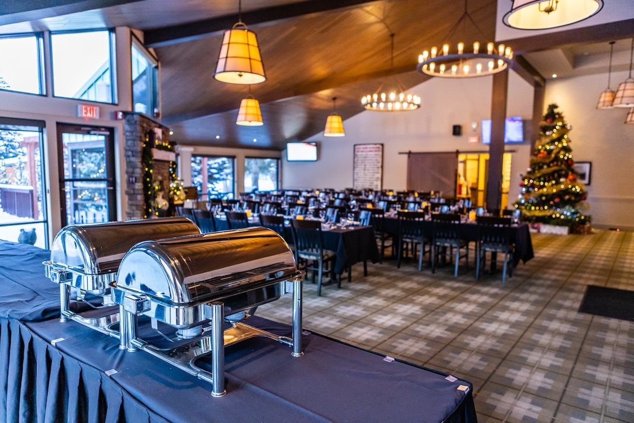 A festive dining hall with a buffet table, set dining tables, and a decorated Christmas tree.
