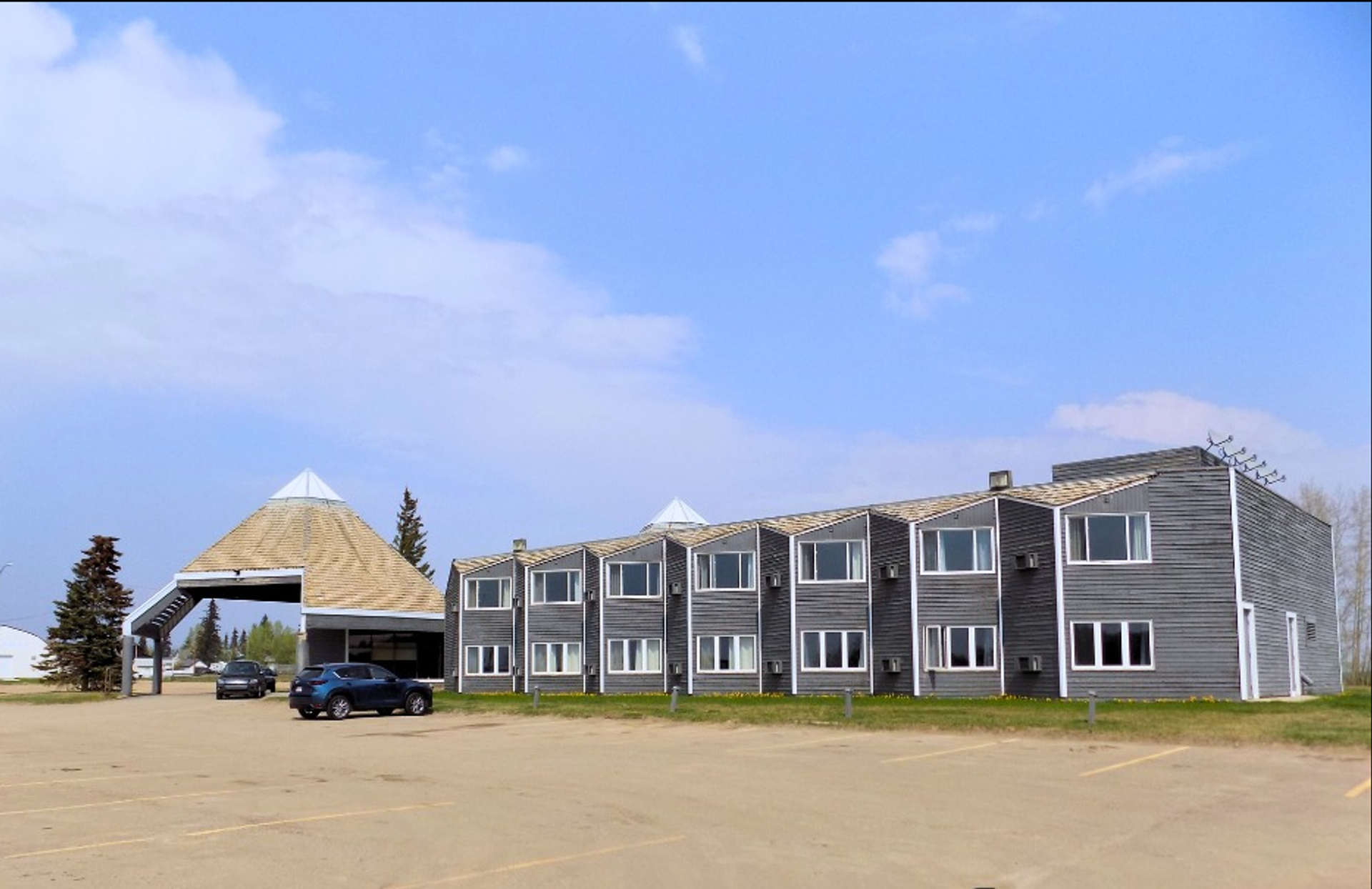 Large two-story inn with unique roof design and parking lot under a clear sky