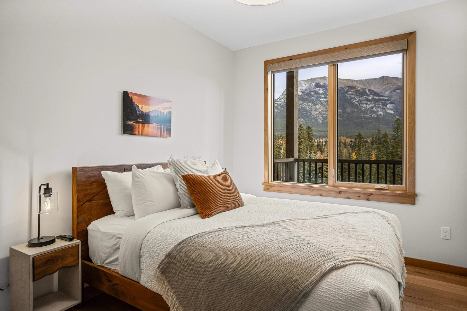 Bedroom with wooden bed and large window overlooking forested mountains.
