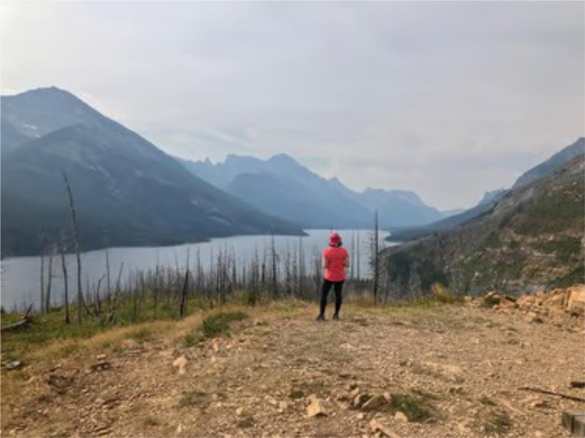 Person stands on a ridge overlooking a mountain lake at sunrise in Waterton.