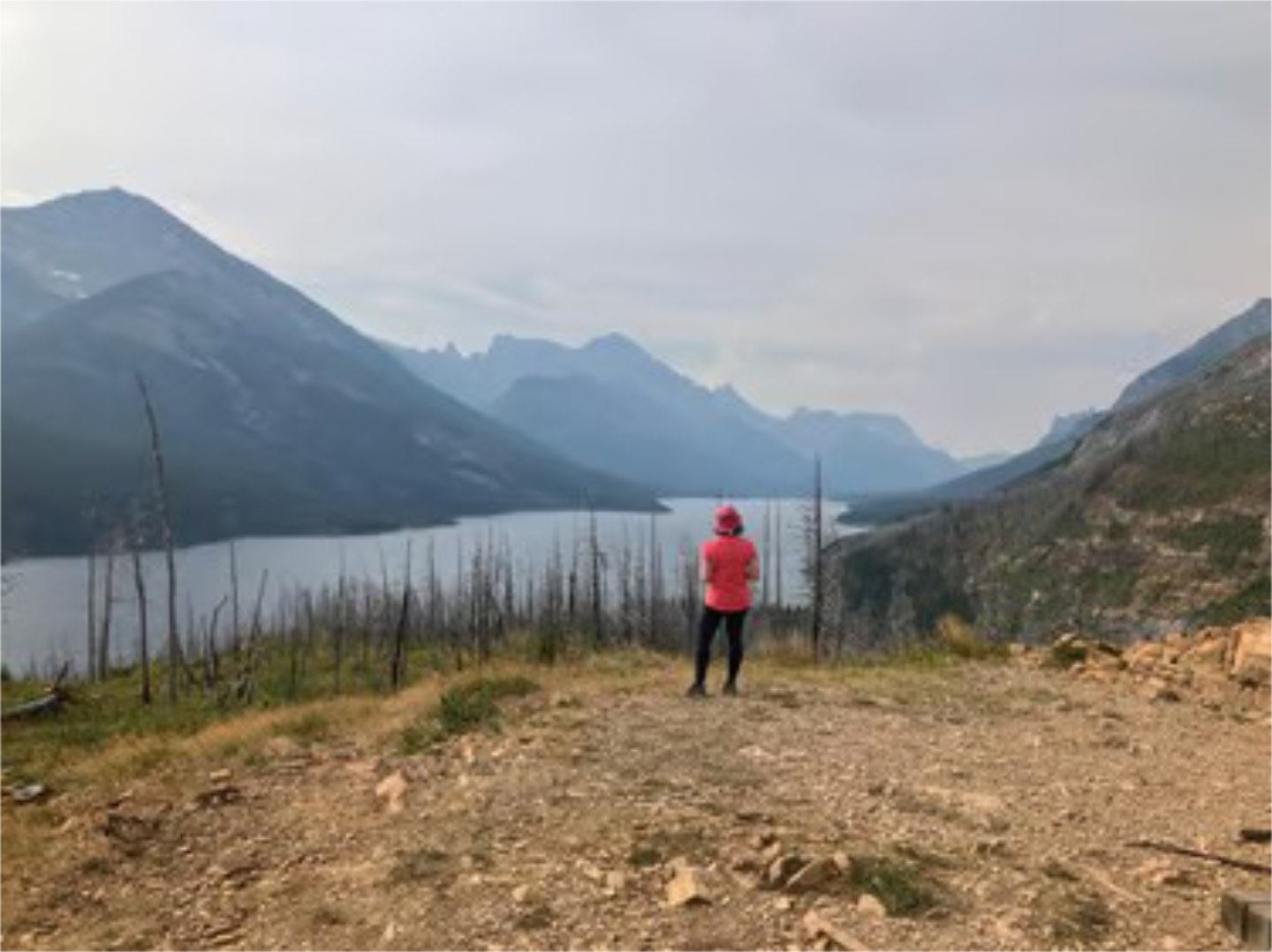 Person stands on a ridge overlooking a mountain lake at sunrise in Waterton.
