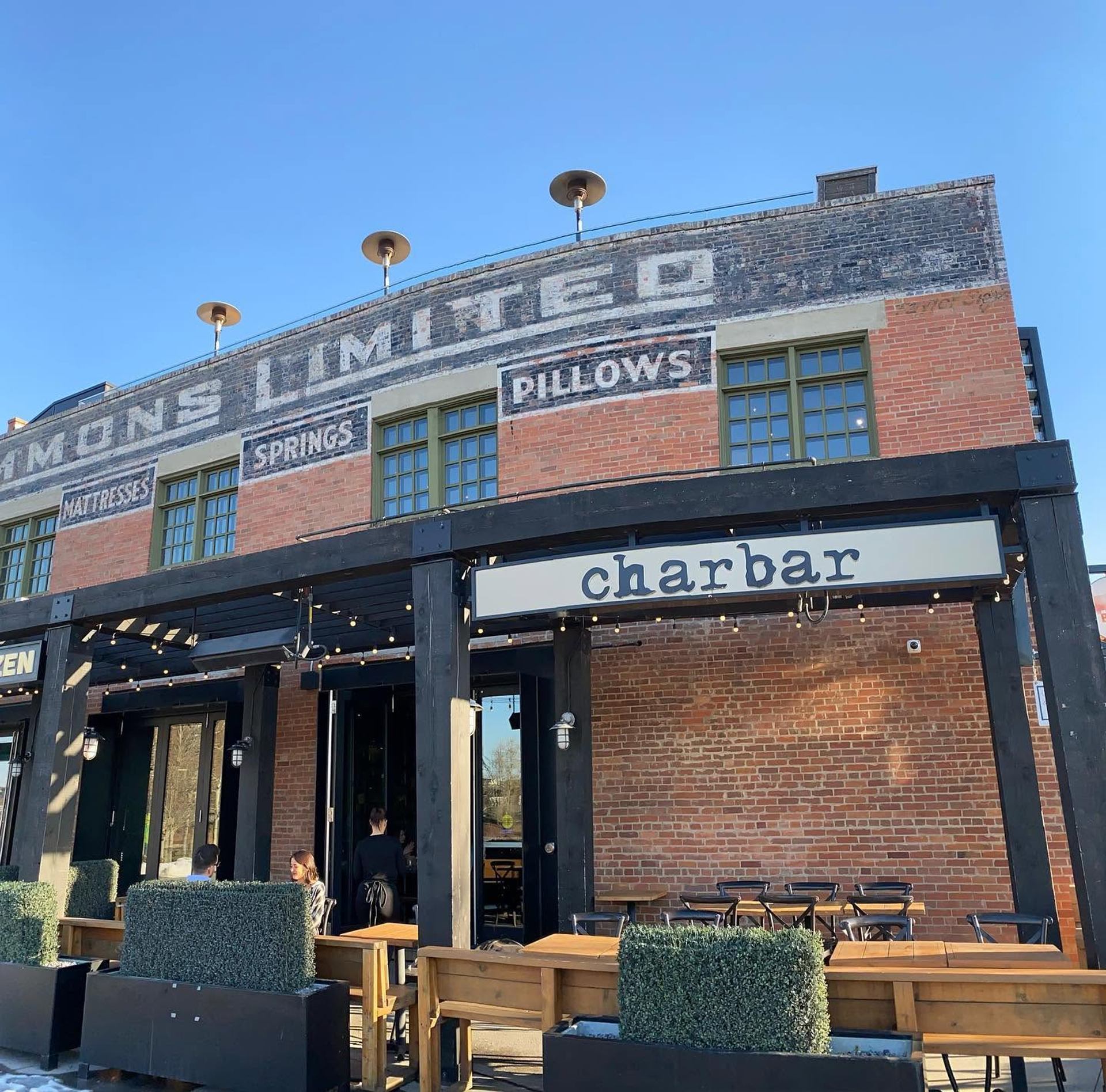 Guests gather outside Charbar, a brick restaurant with patio seating beneath a clear blue sky.  