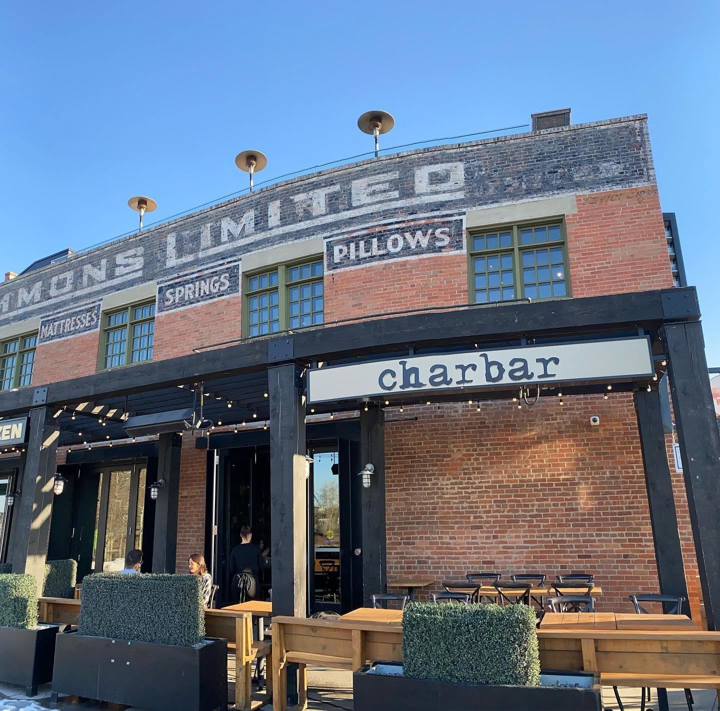 Guests gather outside Charbar, a brick restaurant with patio seating beneath a clear blue sky.