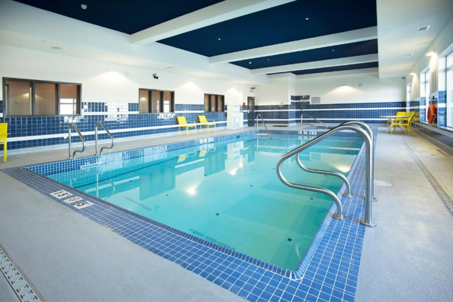 Indoor hotel pool with blue tile, handrails, and seating along the deck.