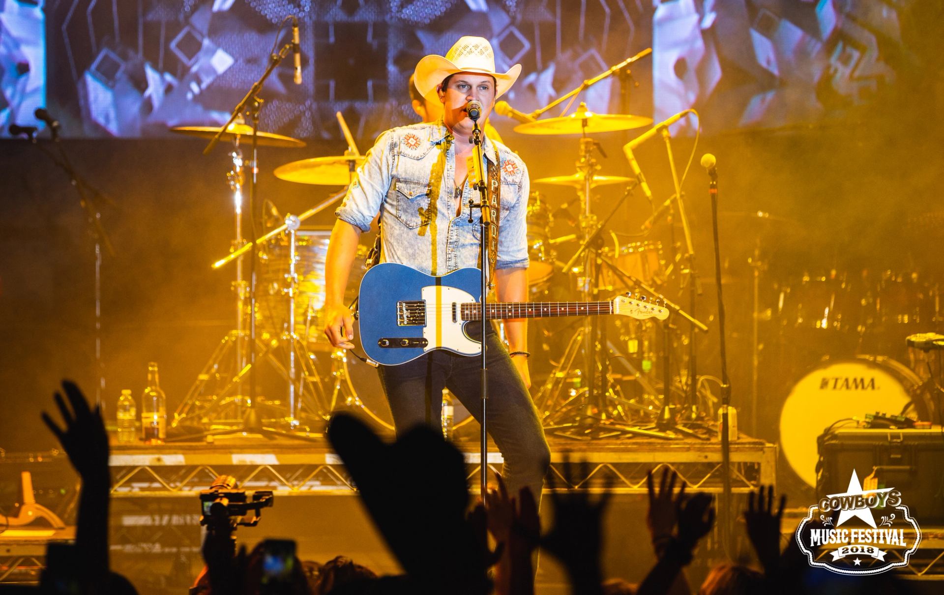 Jon Pardi playing guitar on a brightly lit stage with cheering crowd at Cowboys Music Festival.