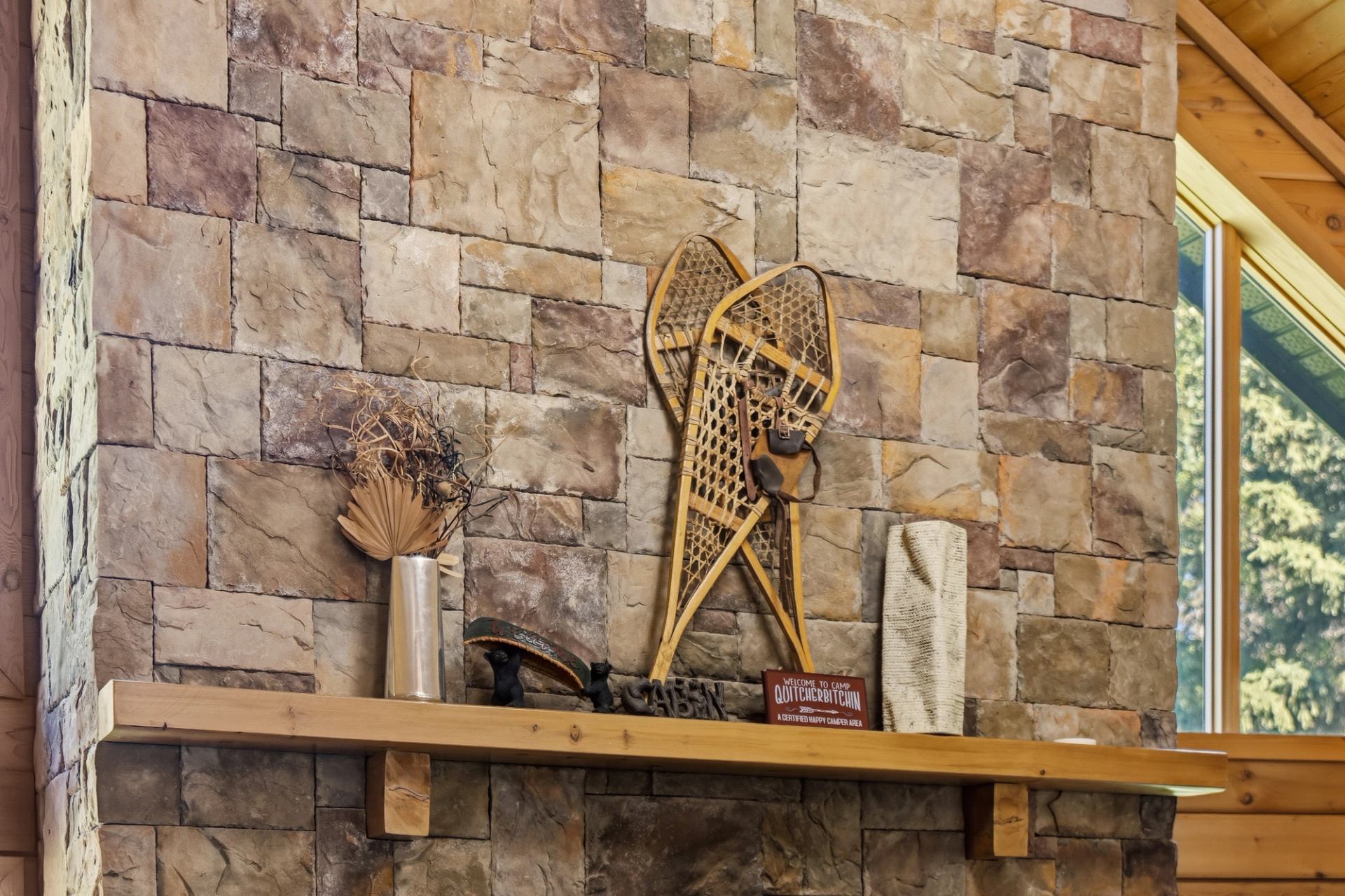 Stone fireplace mantel with vintage snowshoes, dried plants and rustic decorative items.