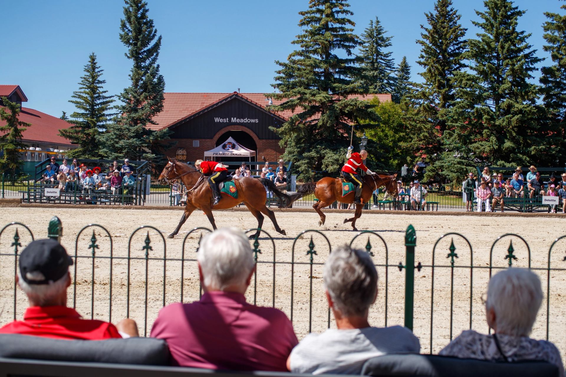 Two uniformed riders on galloping horses perform in an arena before spectators.