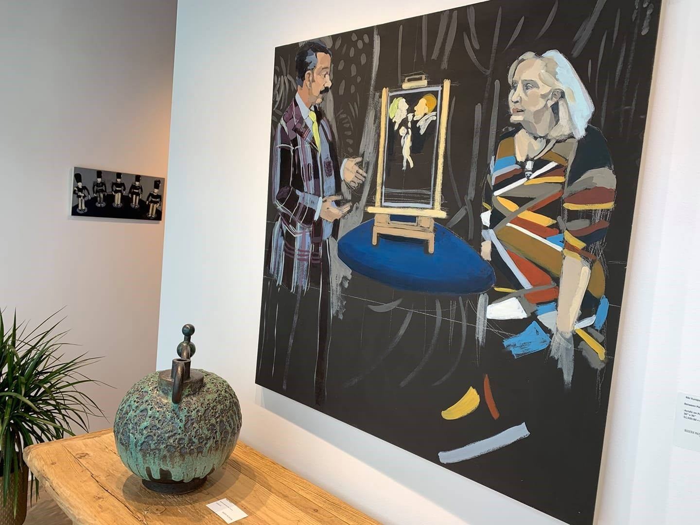Gallery wall with large painting, small artwork and ceramic sculpture on wooden table.