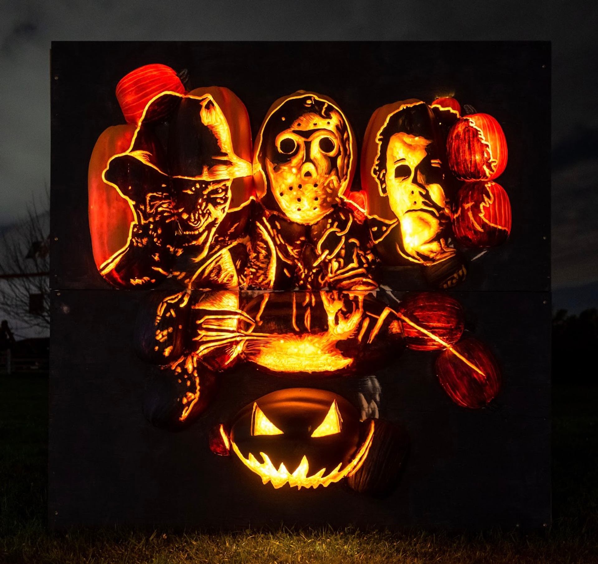 Pumpkin carvings of Freddy Krueger, Jason Voorhees, and Michael Myers glowing in the dark