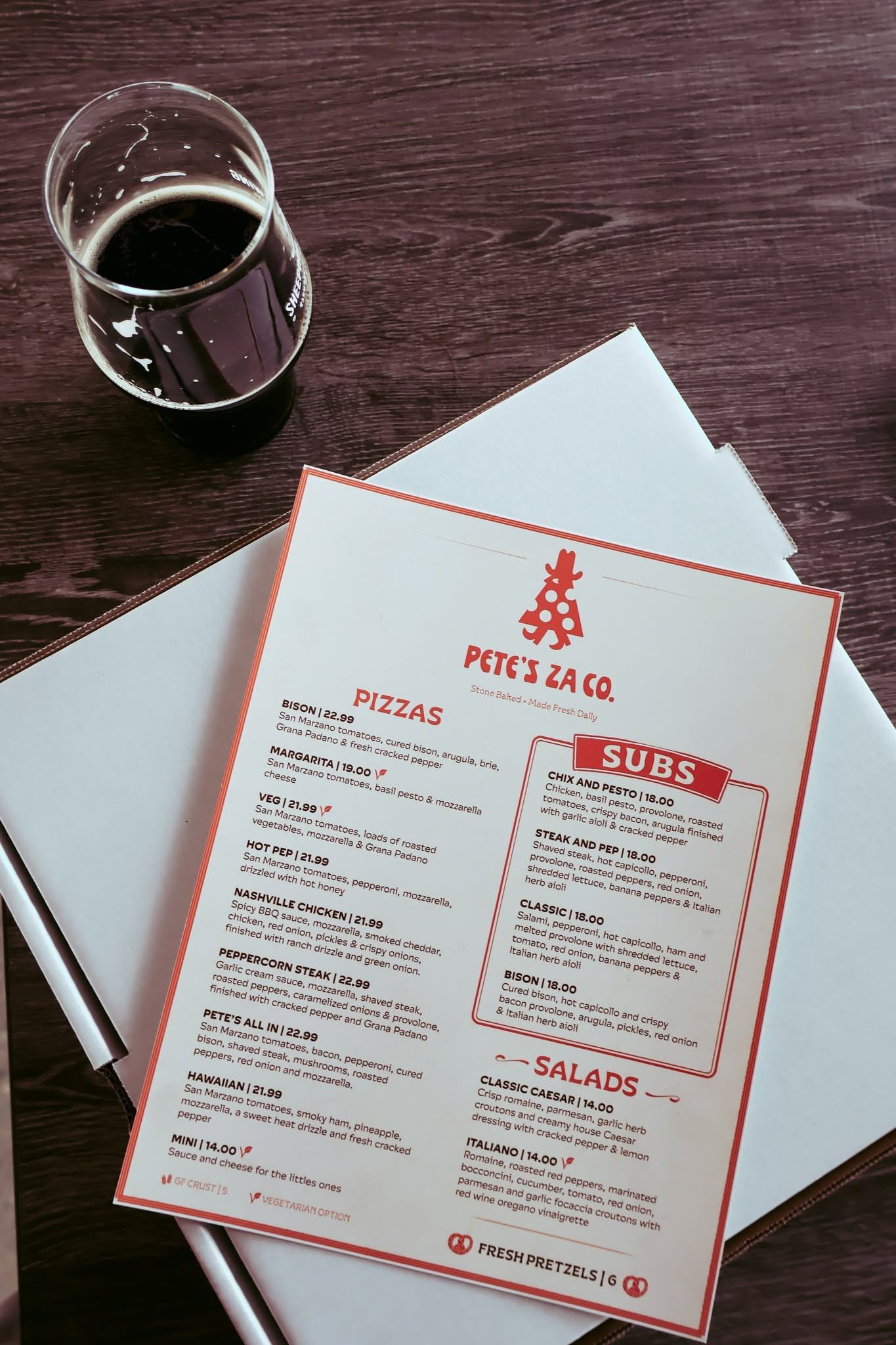 Pete’s Za Co. menu beside a glass of dark beer on a wooden table.