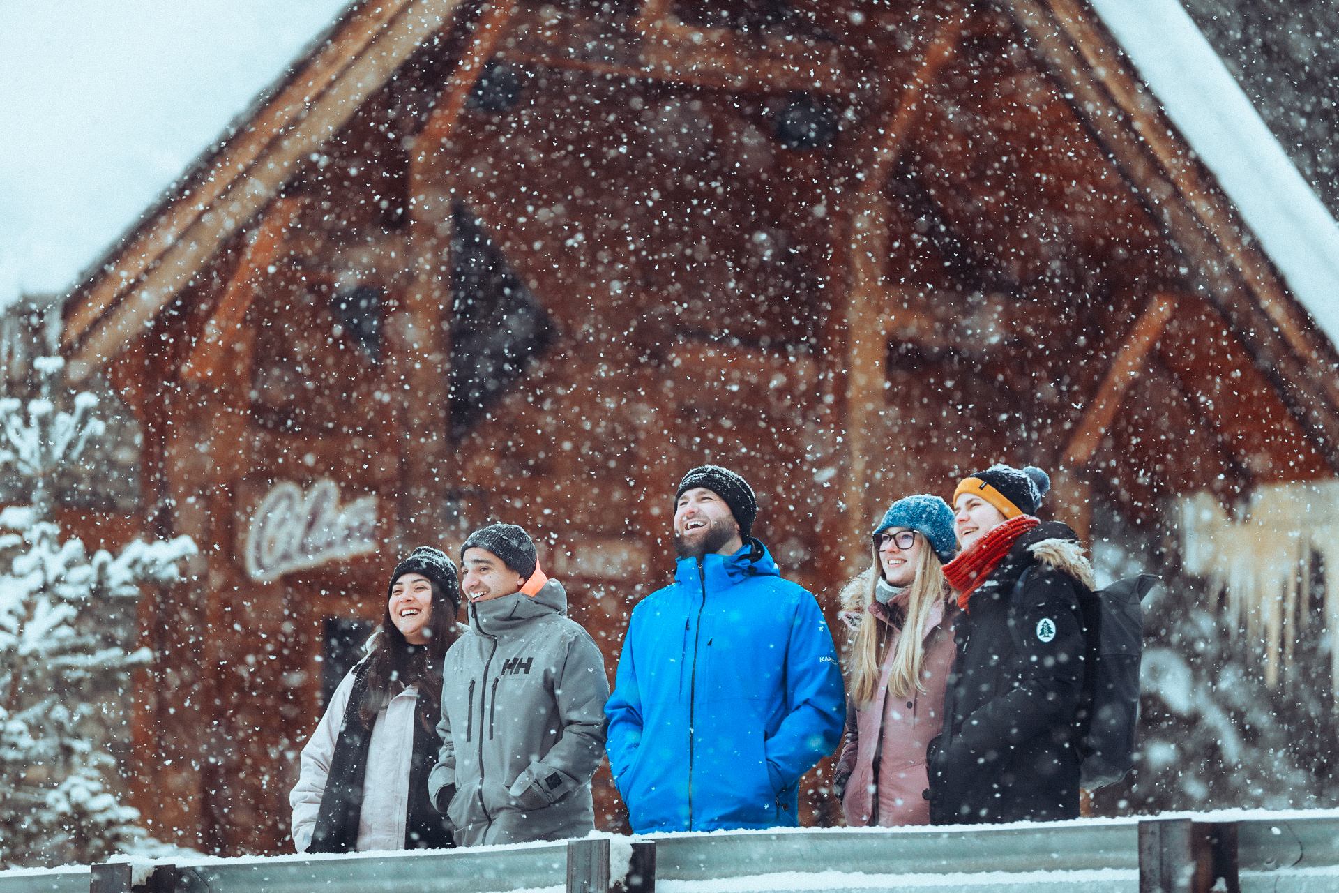 Group standing in falling snow outside a rustic wooden lodge in Banff.