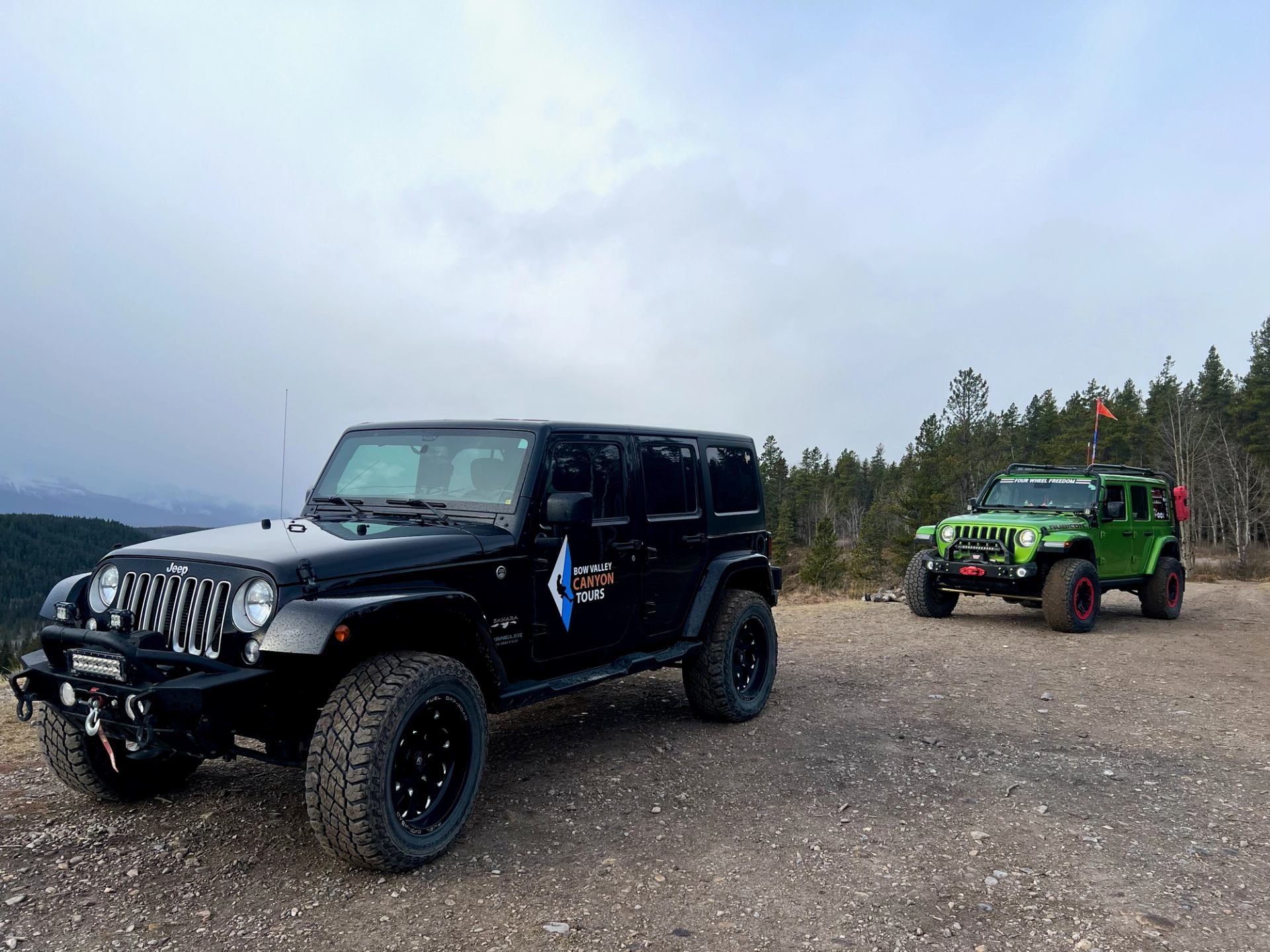 Two rugged Jeeps parked on a mountain trail under cloudy skies.