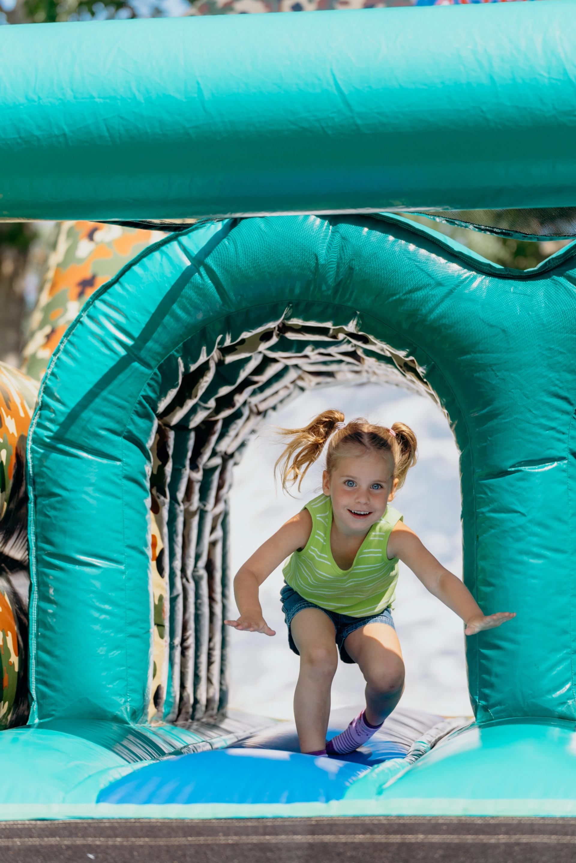 Child moving through a bright teal inflatable tunnel at an outdoor event.