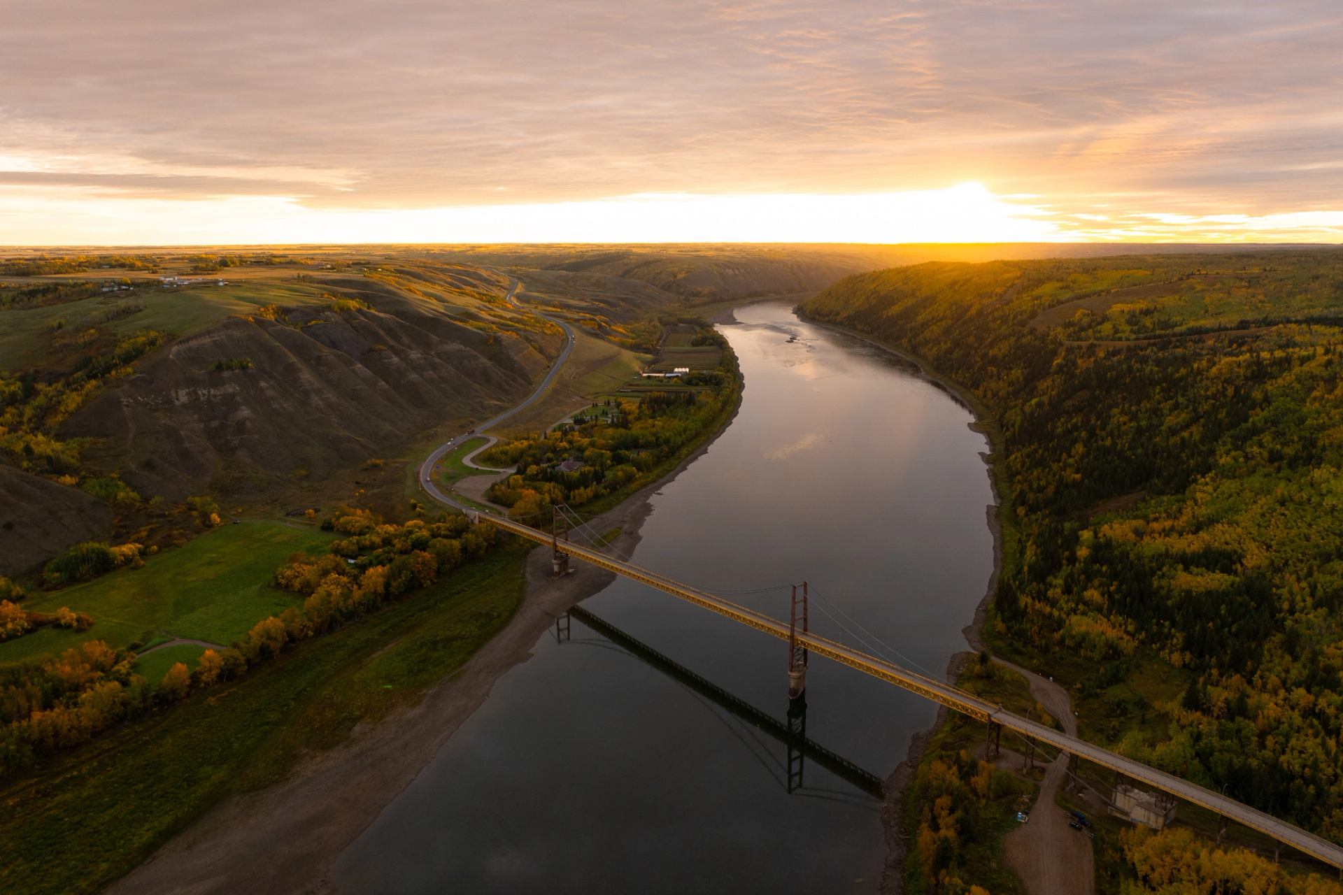Bridge over calm river at sunset, with hills and lush greenery.
