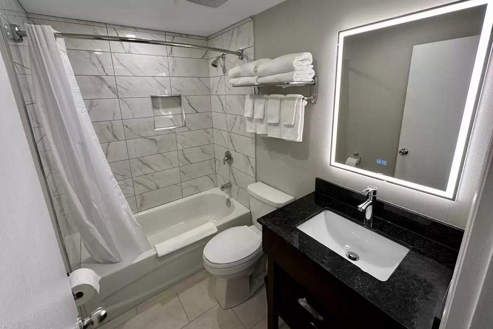 Clean hotel bathroom with tub, toilet, vanity, and marble-patterned tiles.