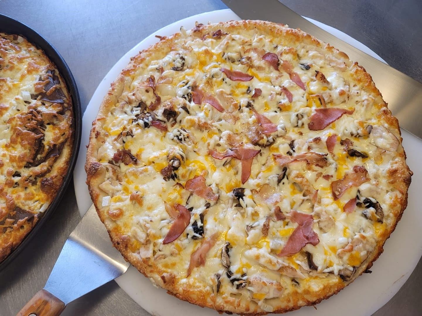 Freshly baked pizza with cheese, ham, mushrooms, and yellow peppers on a white plate.