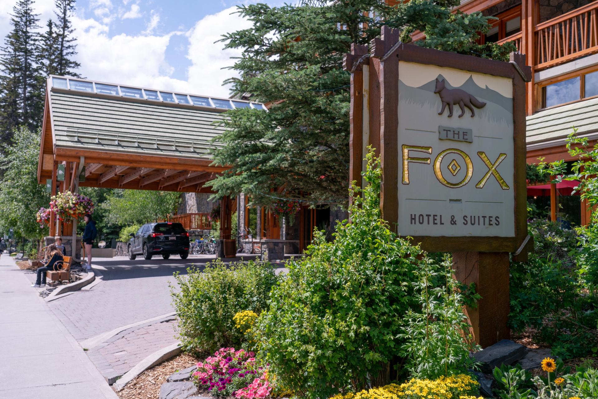 Entrance of Fox Hotel & Suites with rustic sign and lush greenery.