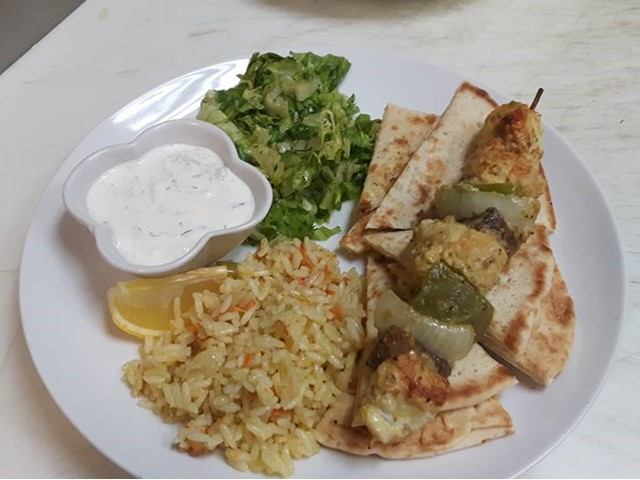 Greek plate with skewered meat, rice, pita, salad, lemon, and tzatziki sauce.