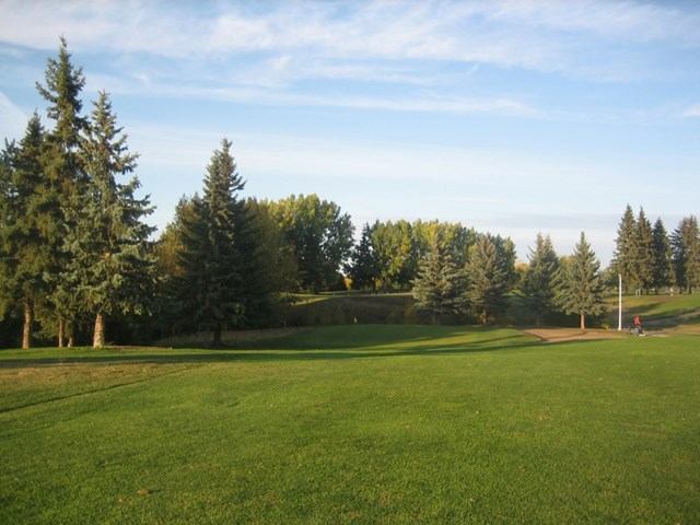 A view of a golf course with trees, green grass, and a person walking in the distance.