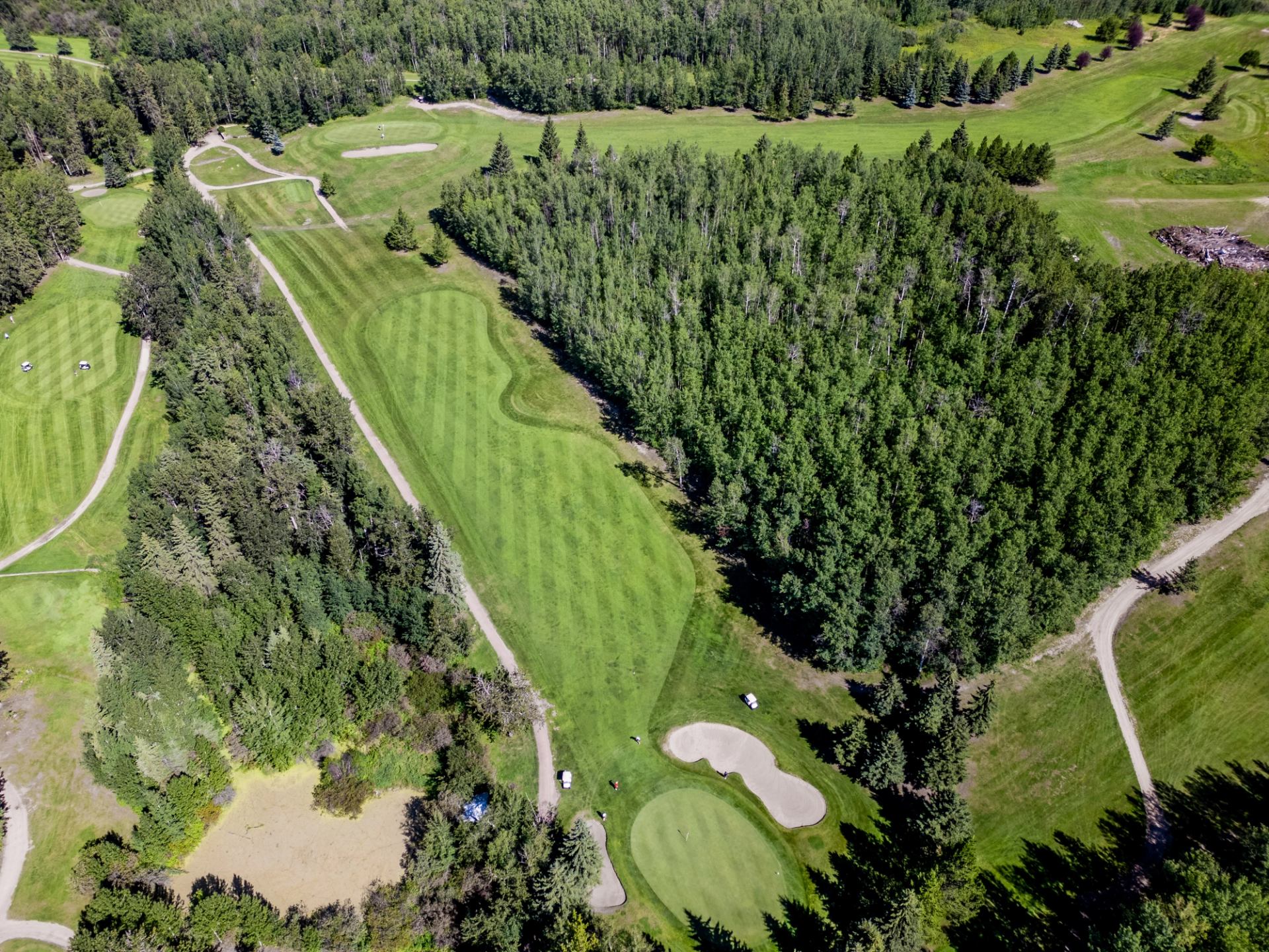 Aerial view of a golf course with fairways, greens, sand traps, and ponds surrounded by dense forest.