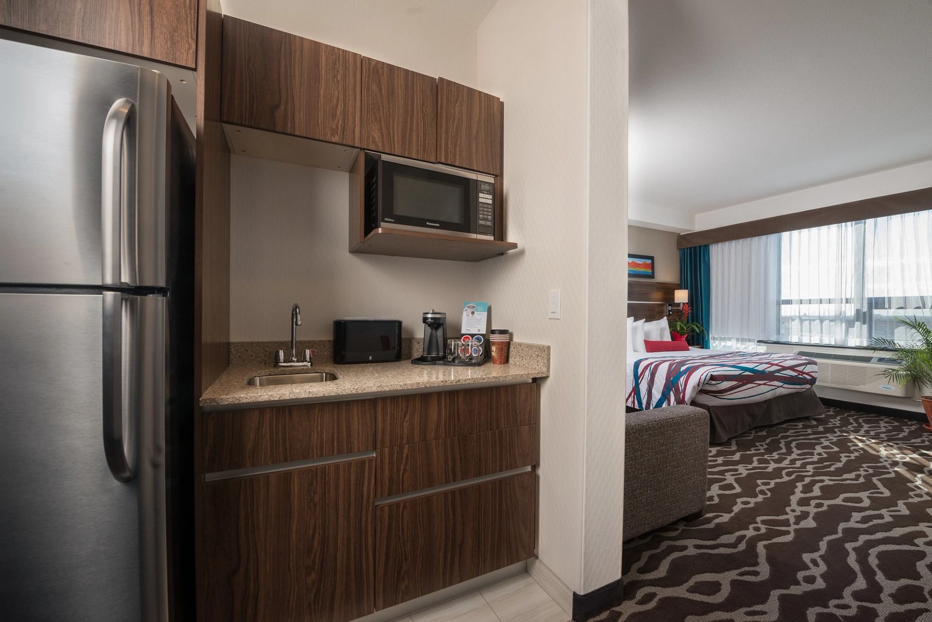 Kitchenette with fridge, microwave, sink, and a view of the bedroom in a hotel suite.