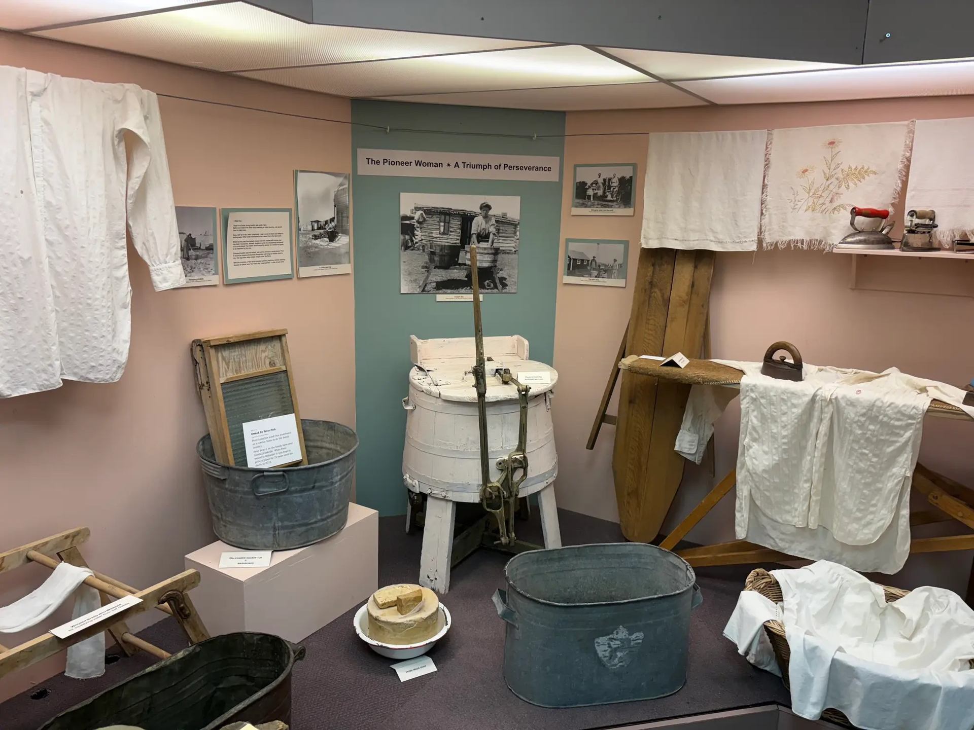 Museum laundry exhibit with wringer washer, wash tubs, ironing board and linens.