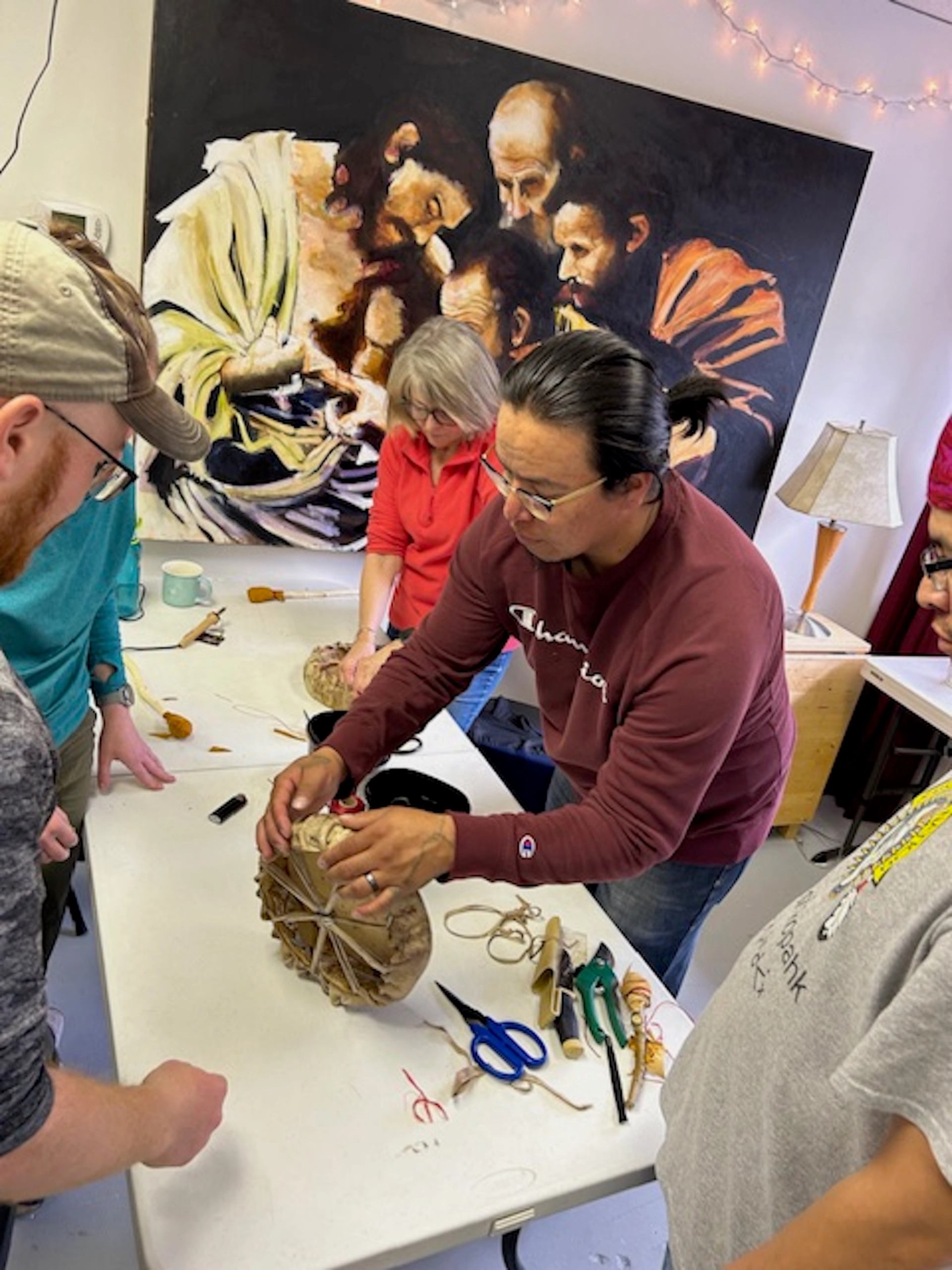 Group crafting with string and spherical object at art-filled table.