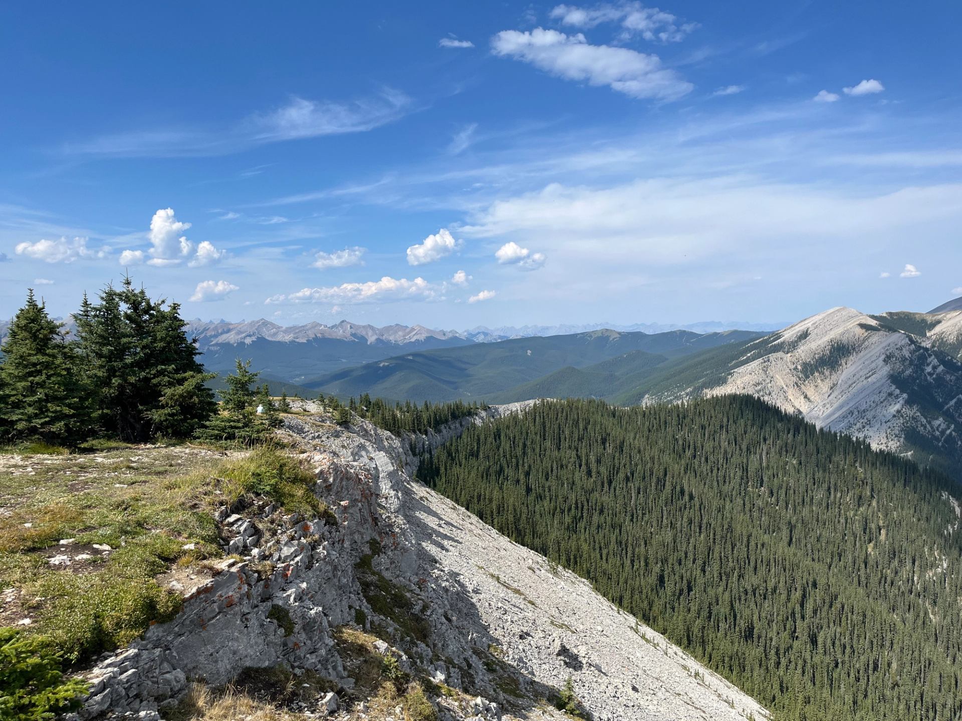 Rocky overlook with dense forest below and mountain ranges stretching into the distance.