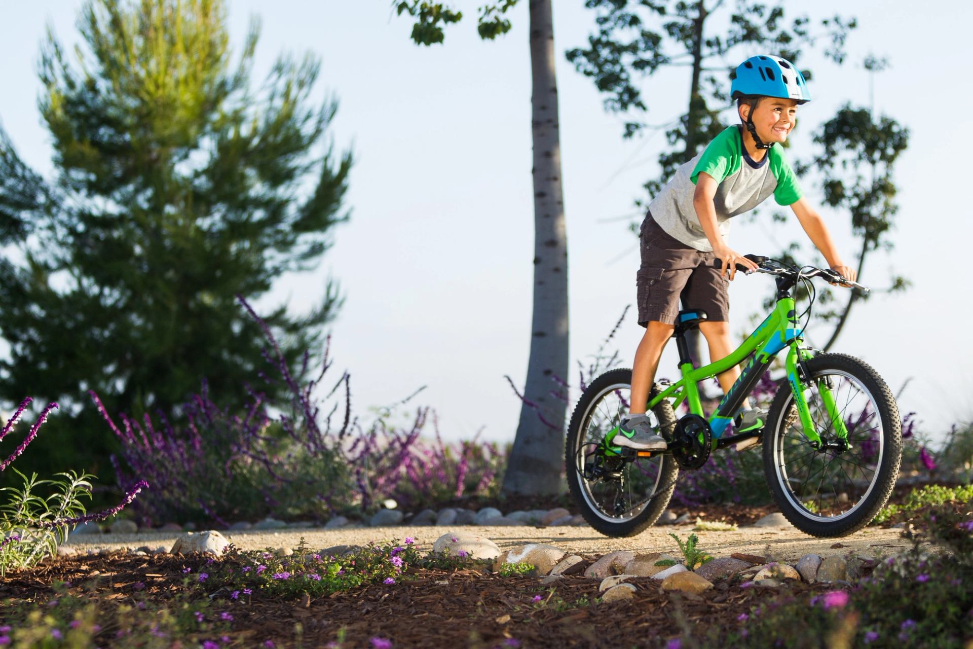 Cyclist on forest trail with purple flowers and green bike.