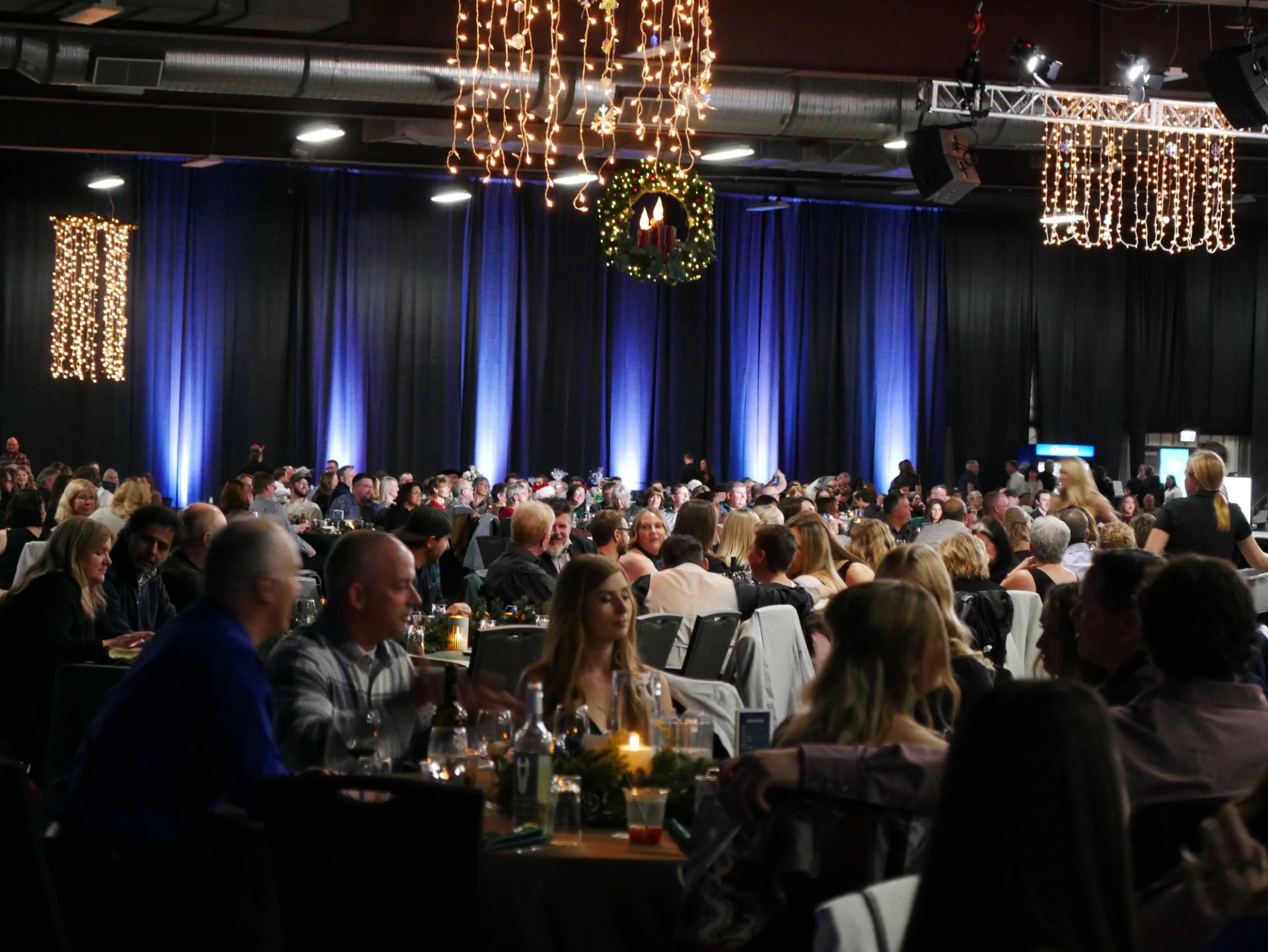 Banquet guests sit at tables beneath hanging lights and a decorated wreath.