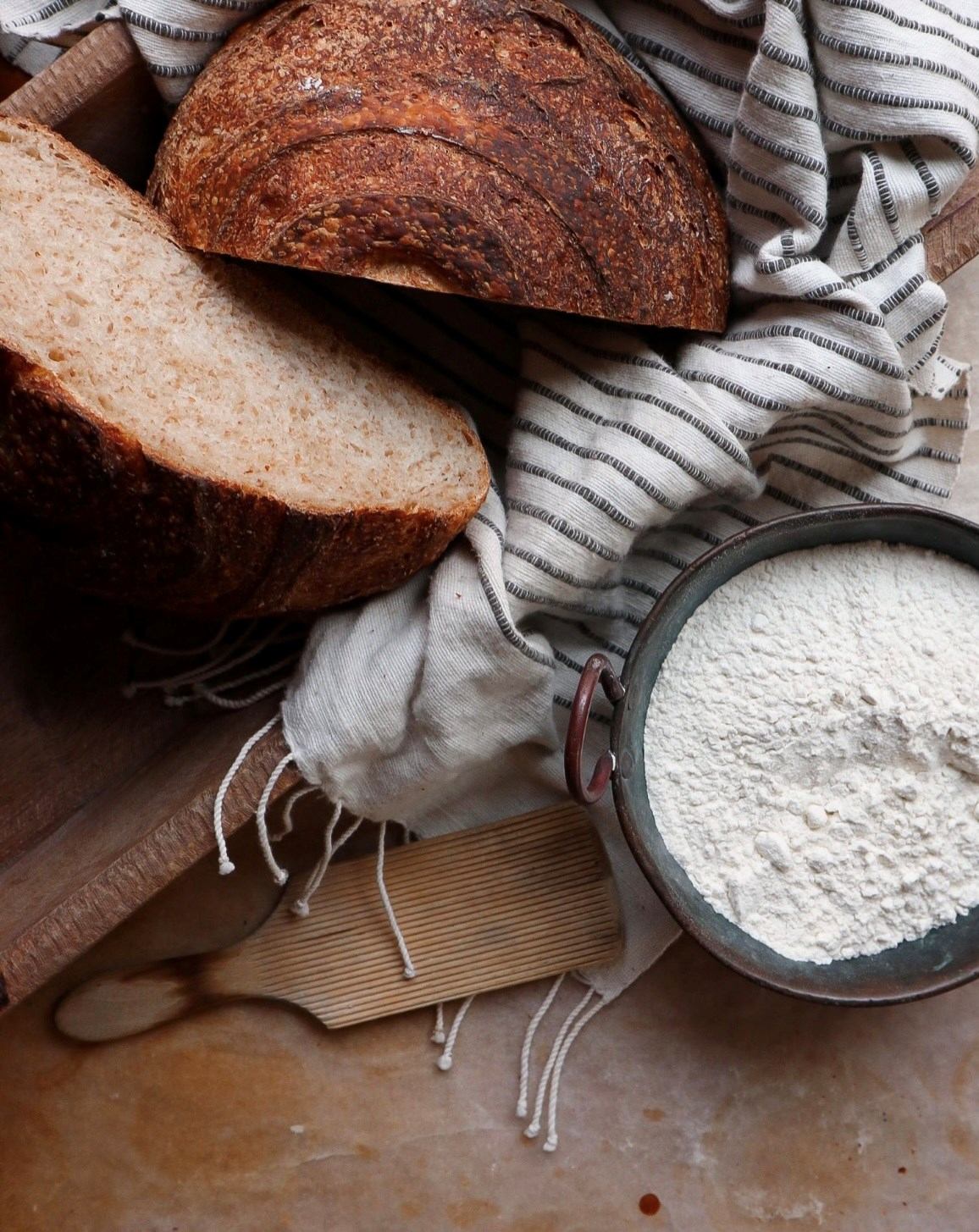 Assorted loaves of bread on striped cloth, with flour in a metal bowl and wooden board.