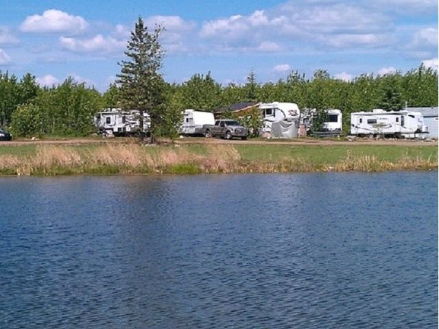 RVs and trailers parked beside a lake, with trees and cloudy sky.