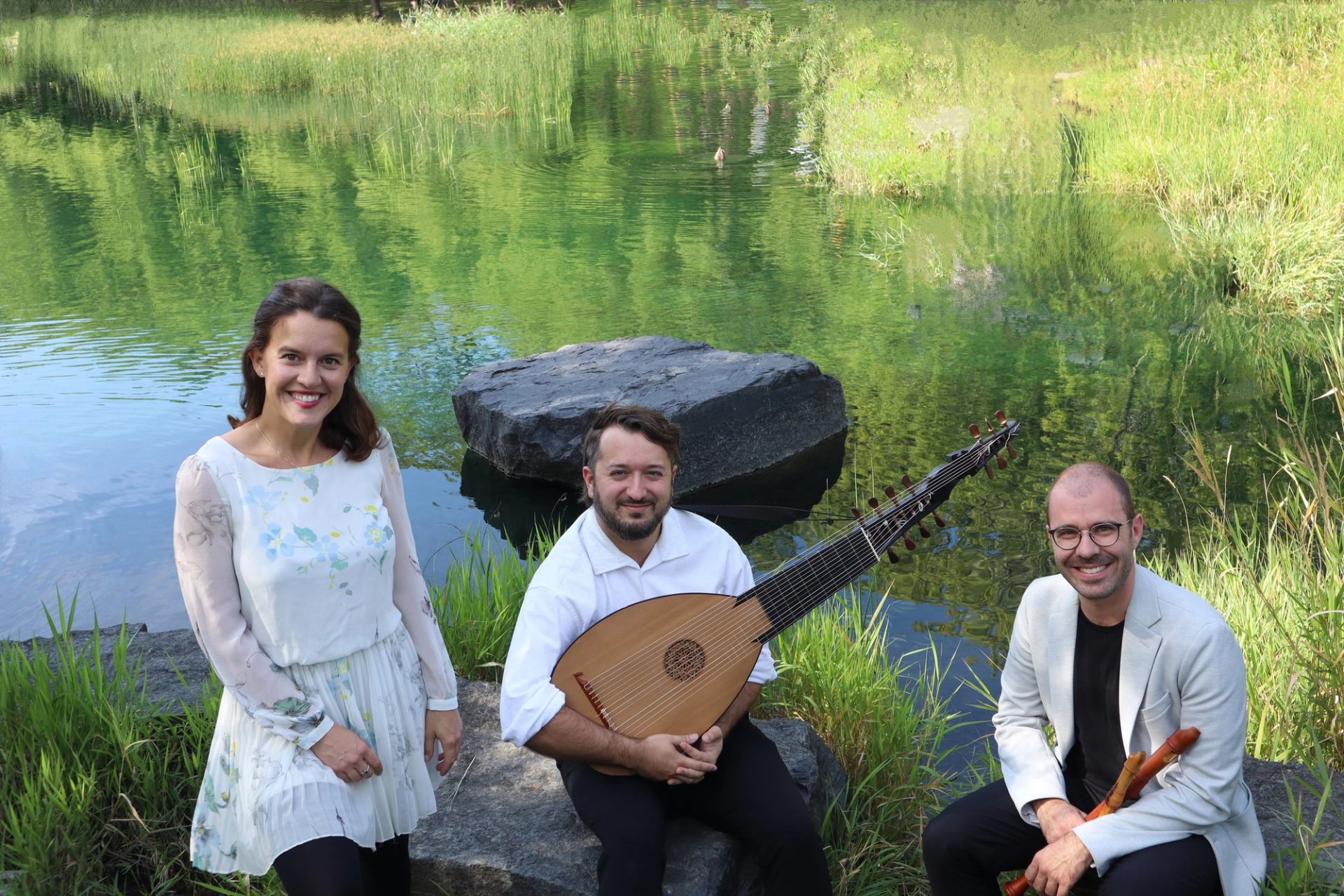 Three musicians sit by a pond, holding a lute and wooden wind instruments.