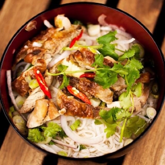 Bowl of noodles topped with grilled chicken, herbs, and chili slices