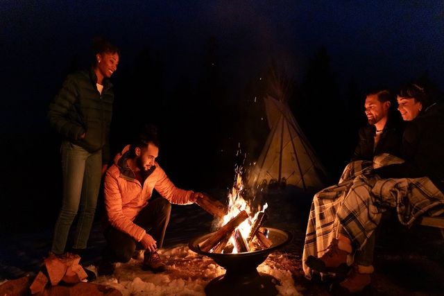 Couples gathered around the campfire in the evening beside a tipi at Running Reins Ranch