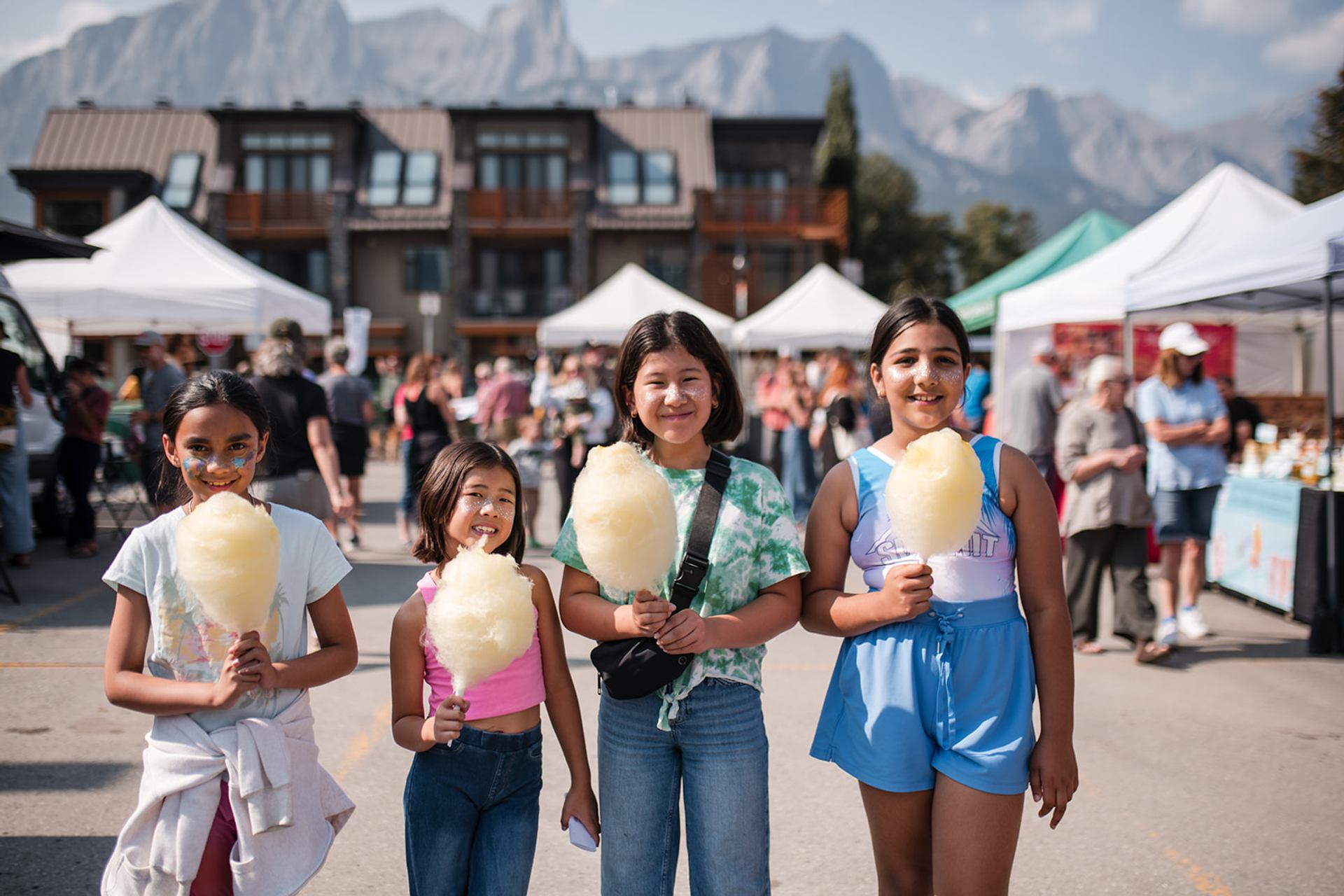 Four girls enjoy cotton candy at an outdoor market.