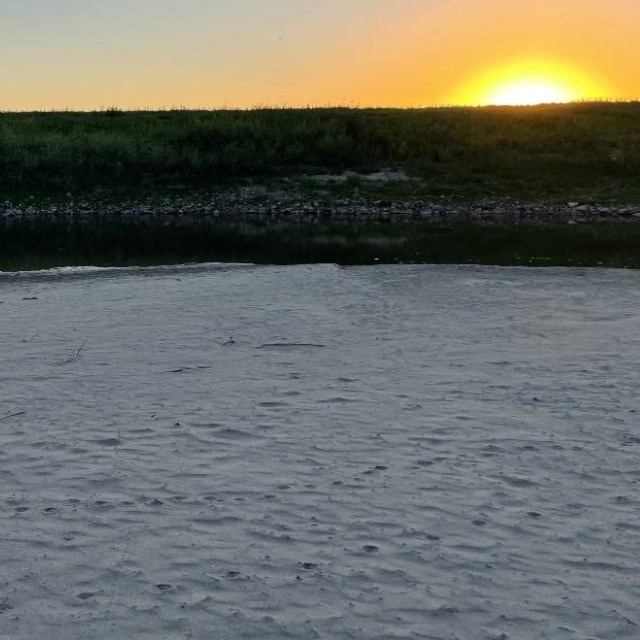 Sunset over a calm river with grassy bank in the background.