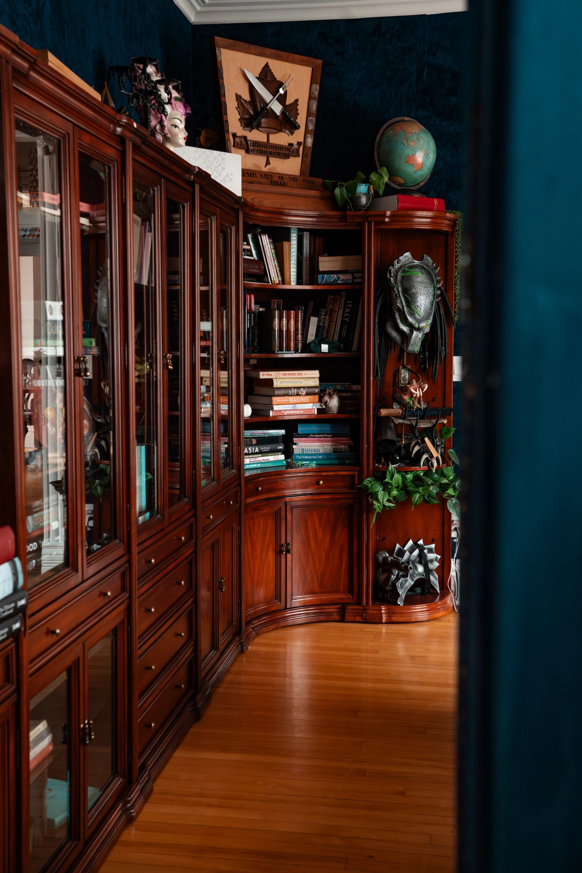 Wooden bookcases with books, globe, decorative helmet and plants along polished floor.